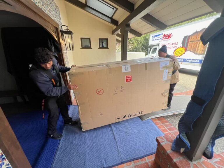 Southbay movers carrying a large boxed item through a front door, with a Southbay truck outside